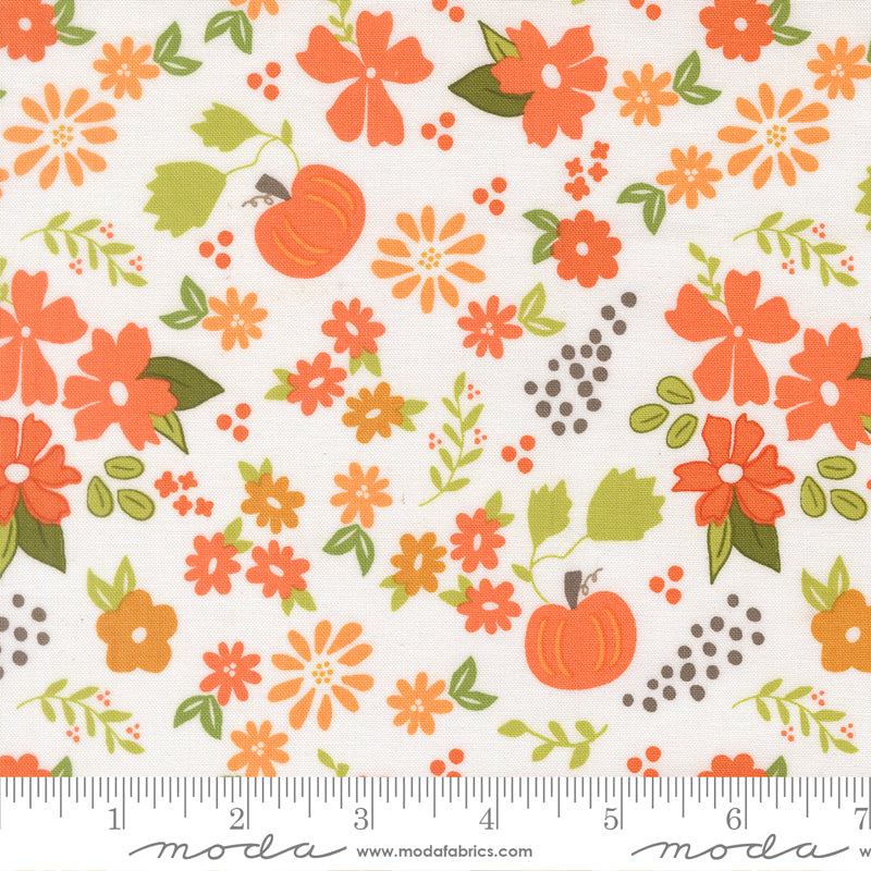 Fabric swatch with orange pumpkins and flowers, green leaves, and orange and grey dots on a white background. Ruler at bottom for scale.