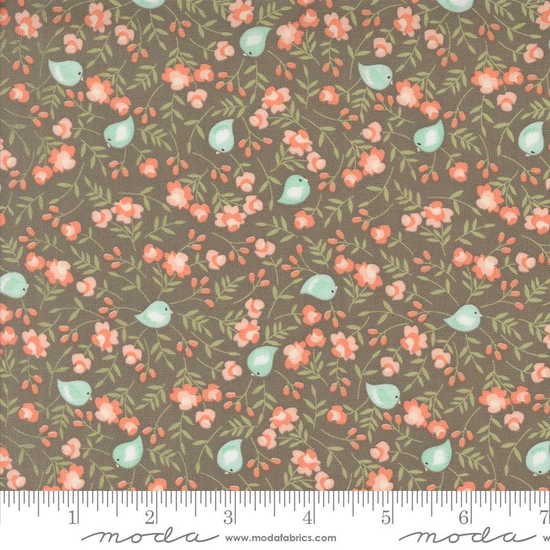 A fabric pattern swatch featuring a slate gray background with a repeating print of small pale blue birds, coral-pink flowers, and green leaves, with a white ruler along the bottom edge showing measurements. The brand name 'modafabrics' is visible at the bottom.