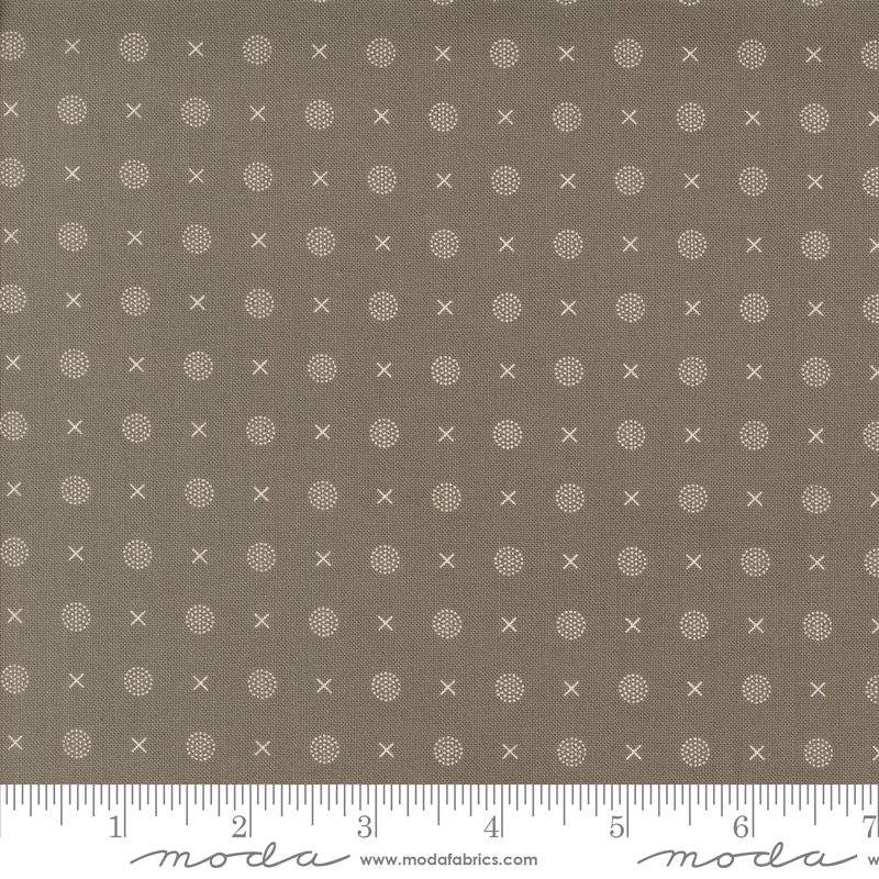 A close-up of a fabric pattern featuring small white x and dot motifs on a slate gray background, with a ruler along the bottom edge showing scale and Modas Fabrics branding.