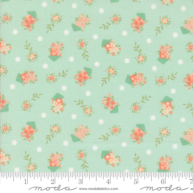 A close-up of a fabric pattern featuring small coral-pink flowers and green leaves in bird houses set against a pale blue background with white polka dots. A white ruler along the bottom edge shows measurements, and the Modas Fabrics logo is printed at the bottom.