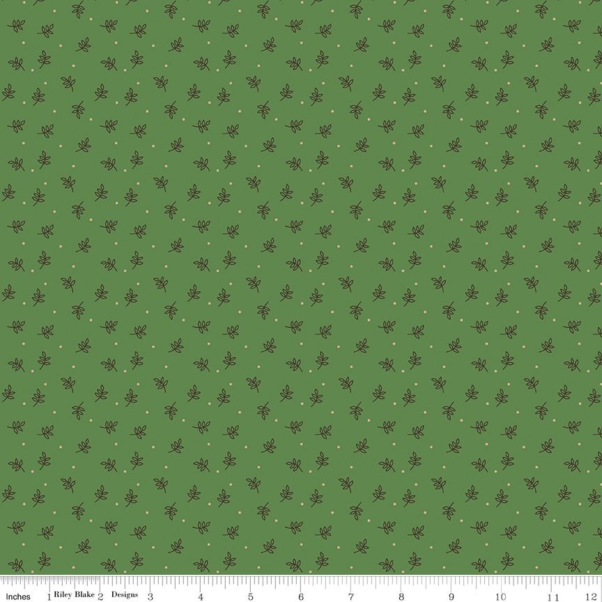 A repeating fabric pattern on a muted green background with small dark brown leaf motifs and tiny light dots, shown with a ruler along the bottom edge for scale.