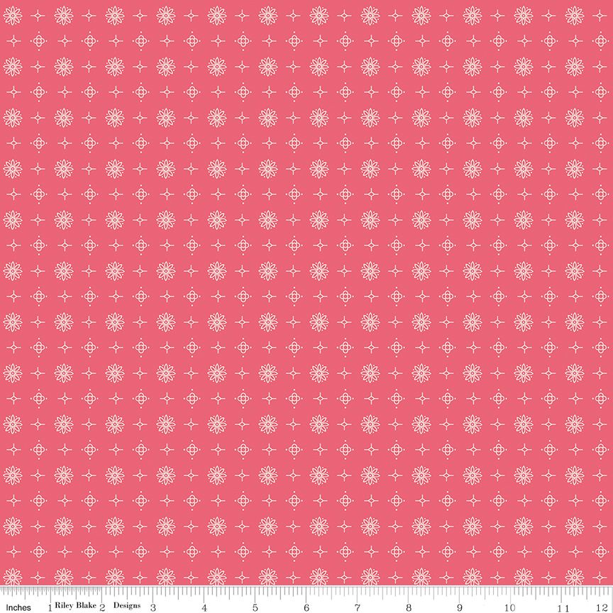 A repeating fabric pattern featuring white snowflakes and small white cross motifs on a solid coral pink background, with a ruler scale at the bottom indicating inches.
