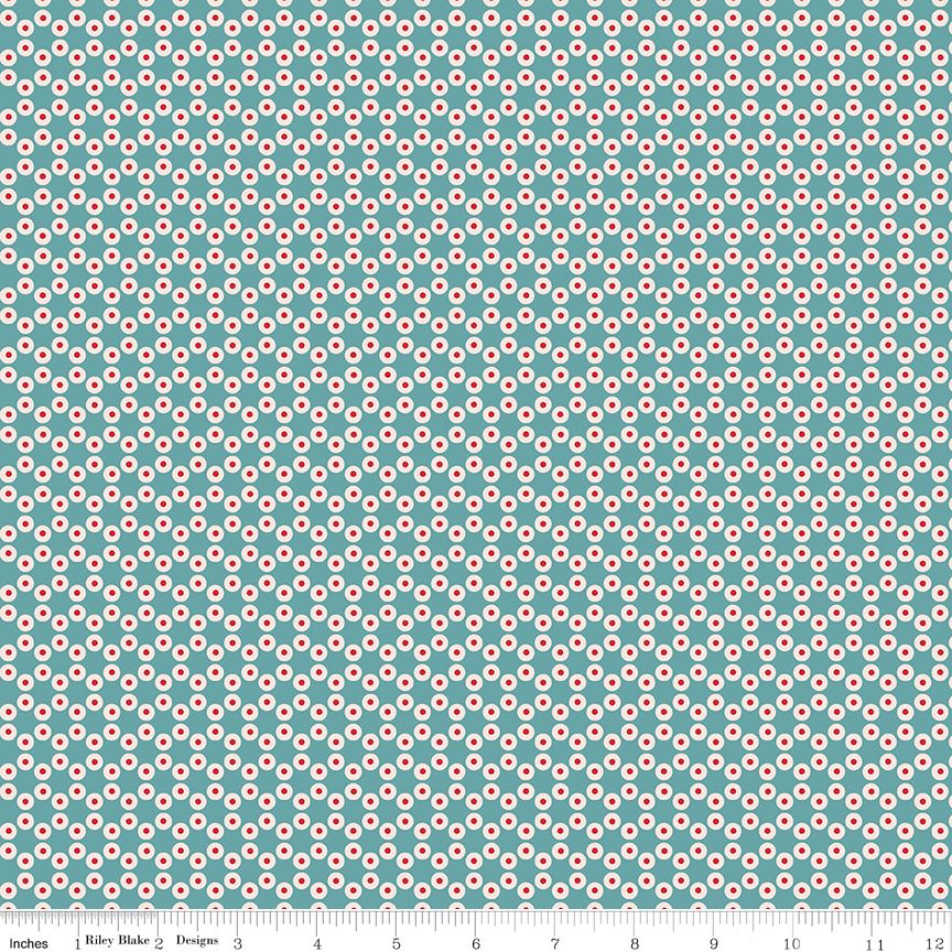 A repeating geometric pattern of small red and white circular motifs on a teal background, with a ruler along the bottom edge showing measurements. The text 'Riley Blake Designs' is visible on the ruler.