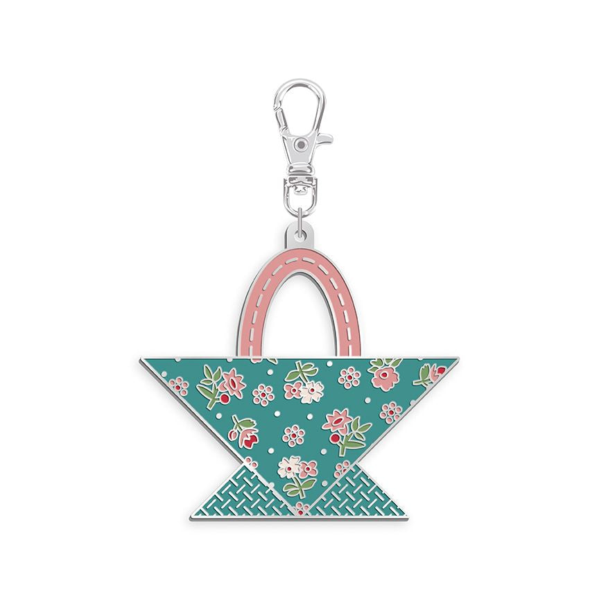 A small decorative keychain bag charm shaped like a handbag, with a silver lobster clasp at the top, a pink handle, and a teal floral body pattern on a white background.