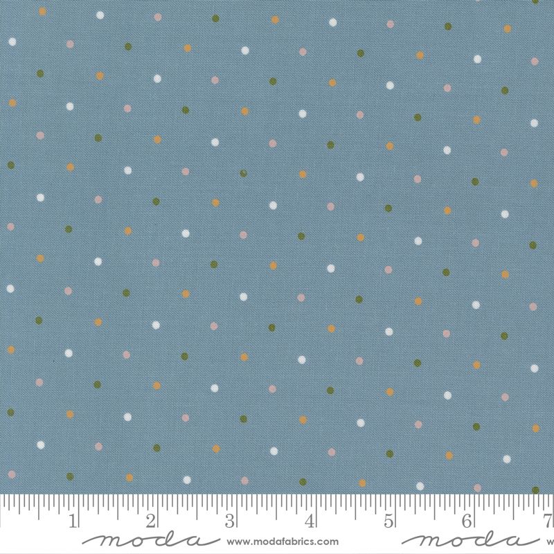 A close-up of a fabric pattern featuring small multicolored polka dots on a dusty blue background, with a ruler at the bottom showing the scale of the print. The brand name 'moda fabrics' is visible on the ruler.
