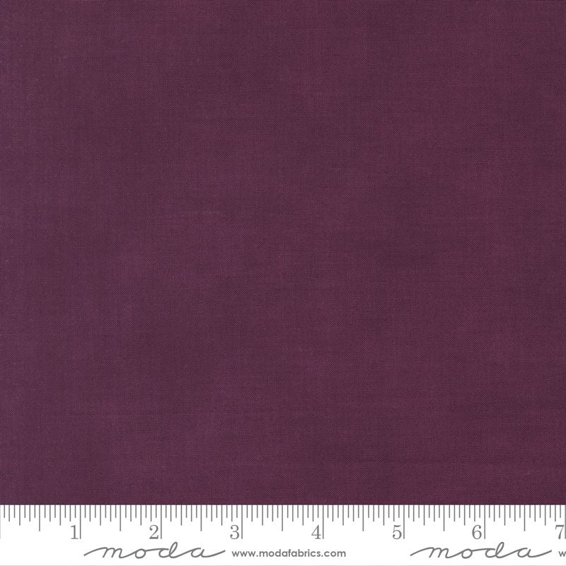 A close-up of a solid deep plum purple fabric texture with a white ruler along the bottom edge showing measurement markings and Modla branding.