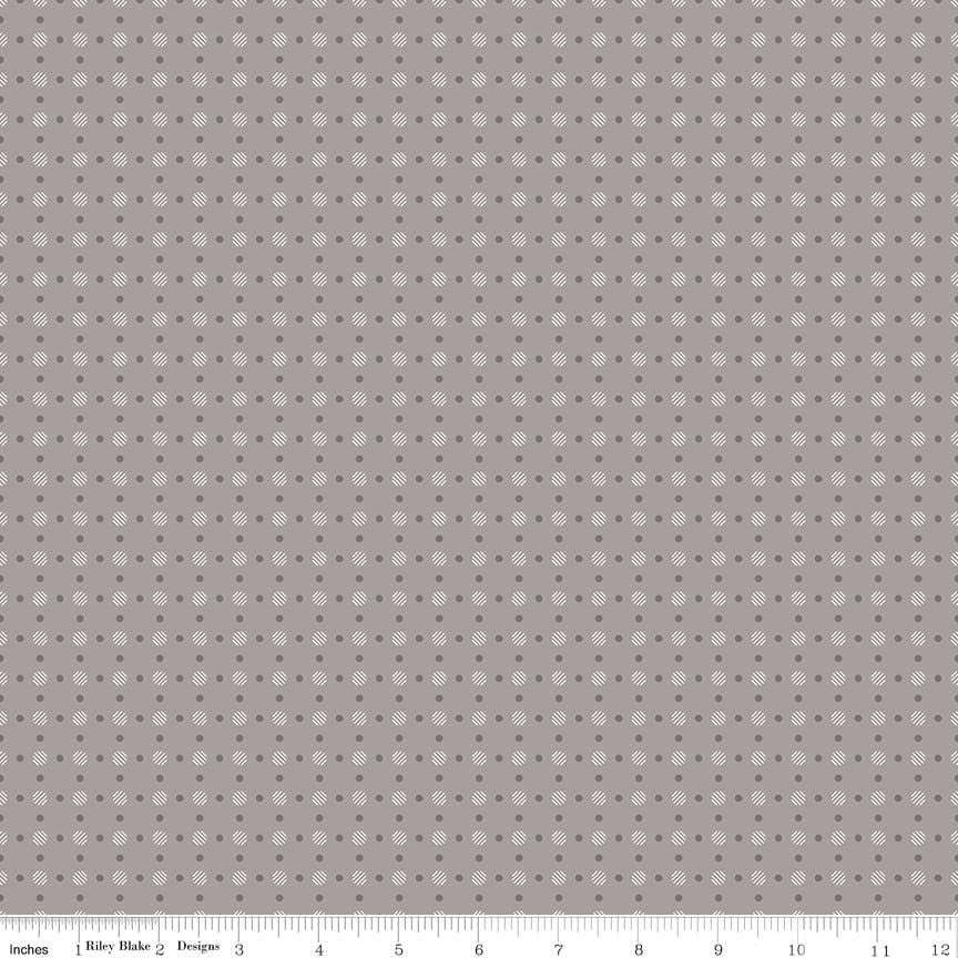 A repeating fabric pattern of small white medallion motifs and dark grey dots on a warm gray background, with a ruler along the bottom edge showing measurements.