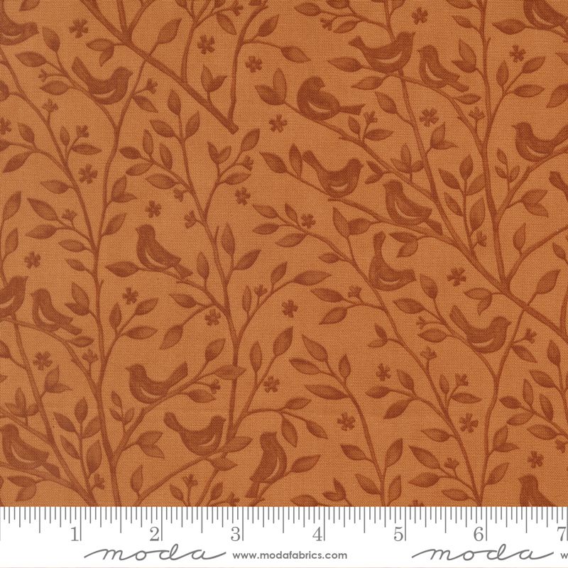 A close-up of a fabric pattern featuring brown birds and leafy branches on a warm rust-orange background, with a measuring ruler along the bottom edge showing scale. The brand name 'moda' is visible on the ruler watermark.