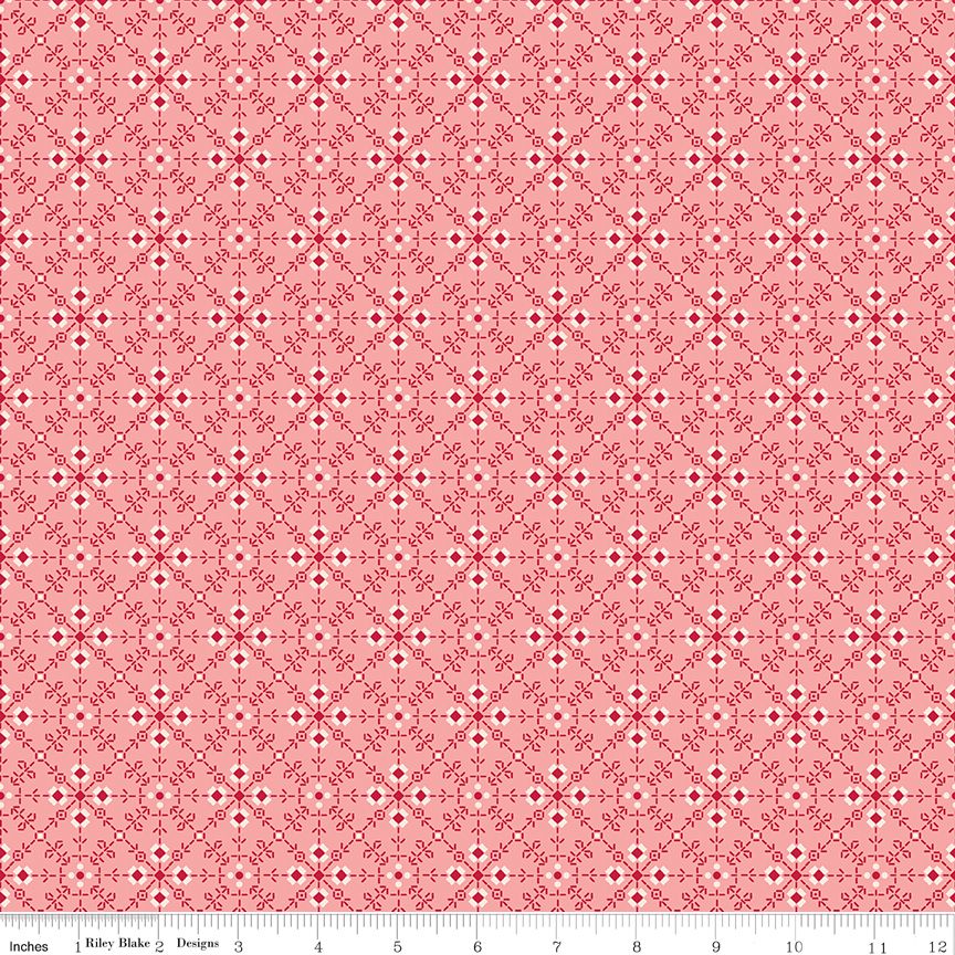 A repeating fabric pattern featuring a red and white geometric medallion design on a light pink background, with a measuring ruler along the bottom edge.