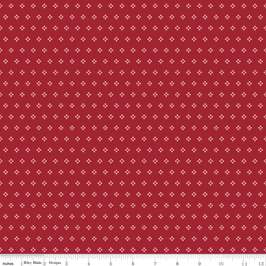 Red fabric with a repeating white geometric pattern, shown flat with a ruler along the bottom edge for scale.