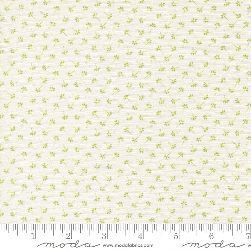 A close-up of a fabric pattern featuring small light green floral motifs on a warm cream background, with a measuring ruler along the bottom edge and Modas Fabrics branding.