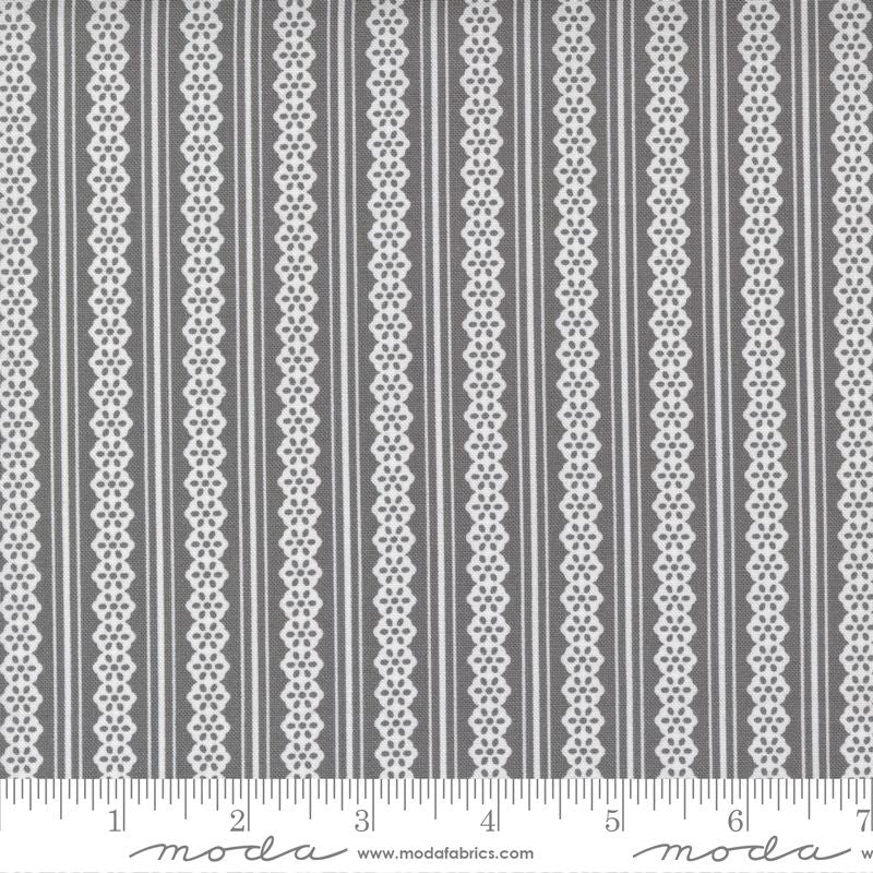 Gray and white striped fabric pattern with vertical bands of solid gray, thin white stripes, and ornate white geometric lace-like motifs. A white ruler along the bottom edge shows measurement markings and a visible Moda watermark.