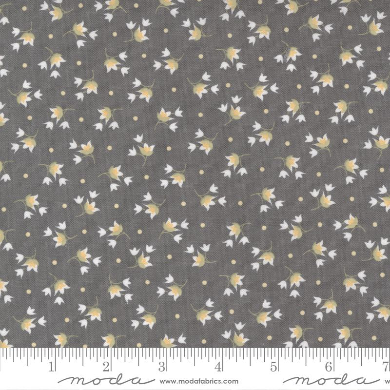 A close-up of a fabric pattern featuring small white flowers with yellow centers and tiny yellow dots on a dark gray background, with a measuring ruler along the bottom edge showing the scale.