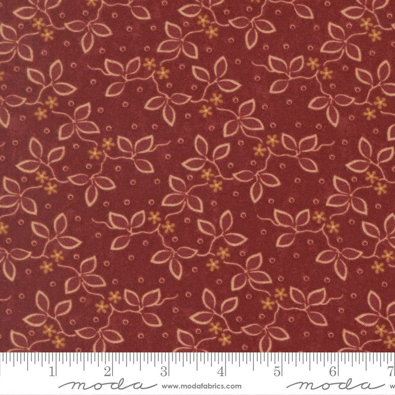 A close-up of a fabric pattern featuring a repeating floral vine design in beige and mustard yellow on a deep reddish-brown background, with a white ruler strip along the bottom edge showing measurements.
