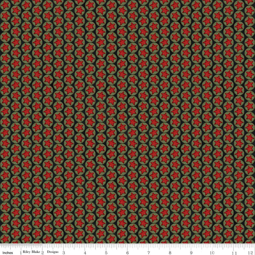 A close-up of a repeating fabric pattern featuring red six-pointed stars inside green six-pointed starbursts, set against a dark olive green background. A white fabric ruler is visible along the bottom edge showing measurements in inches.