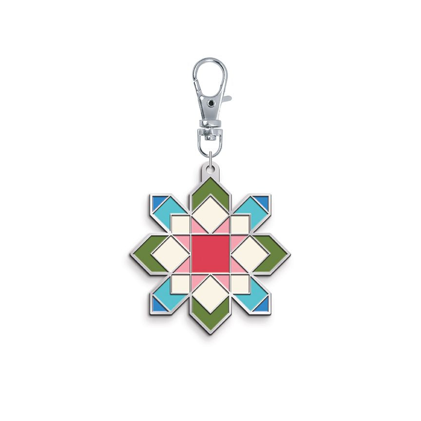 Enamel charm shaped like a quilt star block in pink, green, blue, and cream, on a silver clasp.