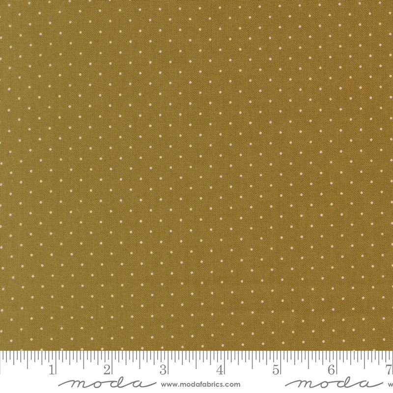 A close-up of a fabric pattern featuring small white polka dots on a warm olive background, with a white ruler along the bottom edge showing measurements and Moda Fabrics branding.
