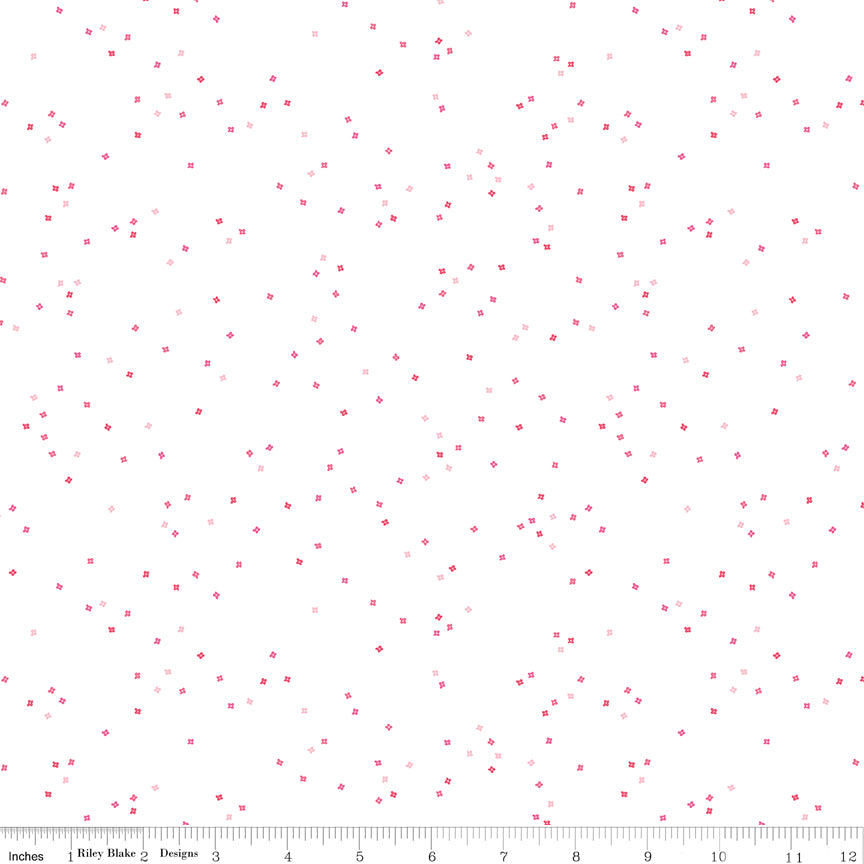 White fabric with tiny blossoms in varying shades of pink with a ruler at the bottom for scale