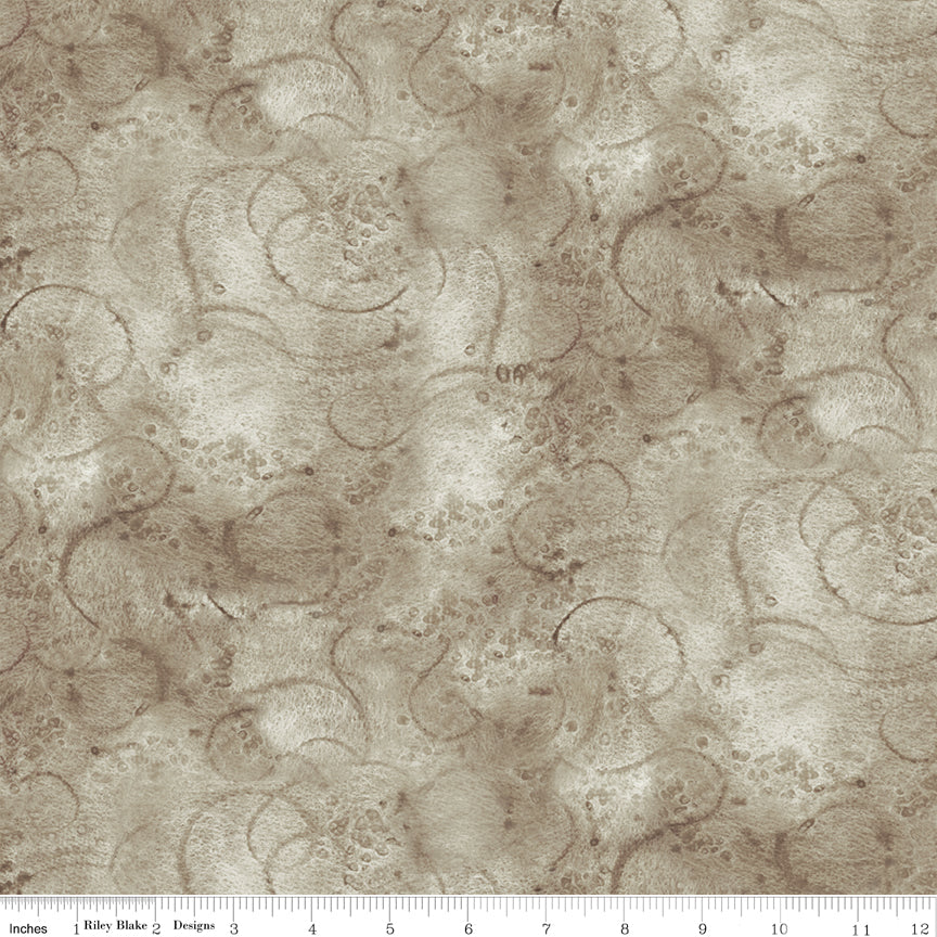 A close-up of a fabric pattern in warm beige and taupe tones, featuring a repeating swirling mottled motif. A small ruler strip is visible along the bottom edge for scale