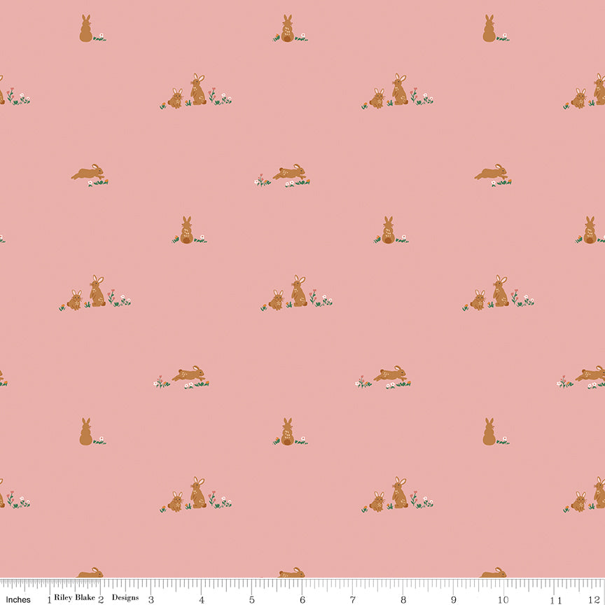 Fabric with a pattern of small bunny illustrations on a pink background with a ruler at the bottom for scale.