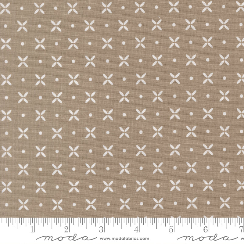 A close-up of a fabric pattern showing a warm taupe-beige background with a repeating white motif of small crosses, dots, and short lines. A ruler along the bottom edge shows scale, and the Modafabrics watermark is visible at the bottom.