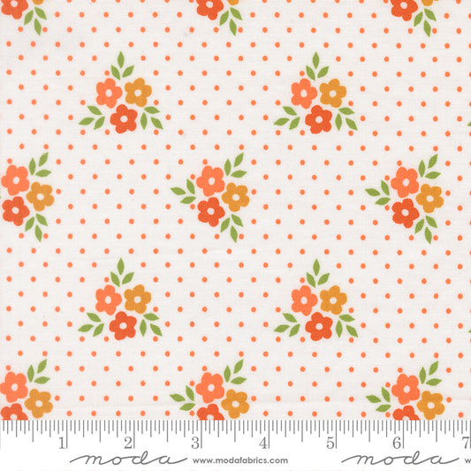 White fabric featuring orange and yellow flowers and orange polka dots.  Ruler at the bottom for scale.