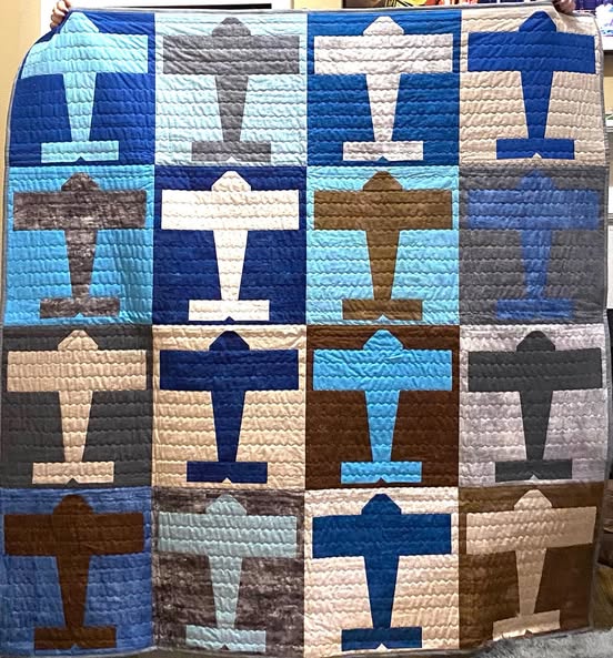 A handmade quilted patchwork blanket featuring a grid of airplane shapes in various colors including blue, brown, beige, and gray.