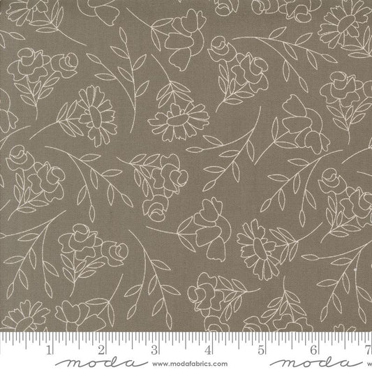 A close-up of a fabric pattern featuring delicate white floral and leaf line drawings on a warm slate gray background, with a ruler along the bottom edge showing the scale.