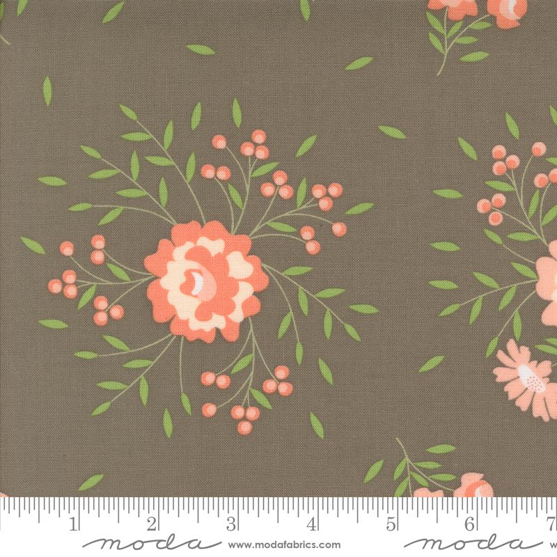 A close-up of a fabric pattern featuring coral-pink and cream flowers, green leaves, and small pink berries on a slate gray background, with a measuring ruler along the bottom edge showing the scale.