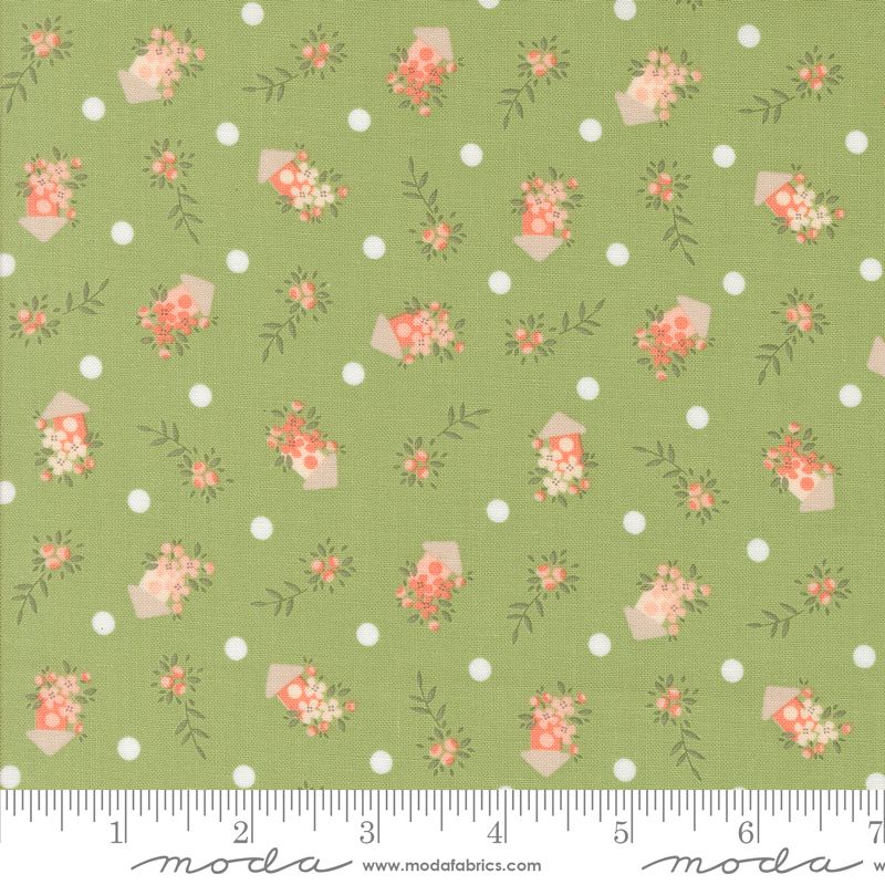 A close-up of a fabric pattern featuring a sage green background with white polka dots and small floral bouquets in coral, pink, and cream birdhouses, with a measuring ruler along the bottom edge showing the scale.