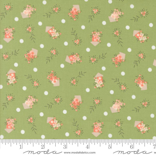 A close-up of a fabric pattern featuring a sage green background with white polka dots and small floral bouquets in coral, pink, and cream birdhouses, with a measuring ruler along the bottom edge showing the scale.