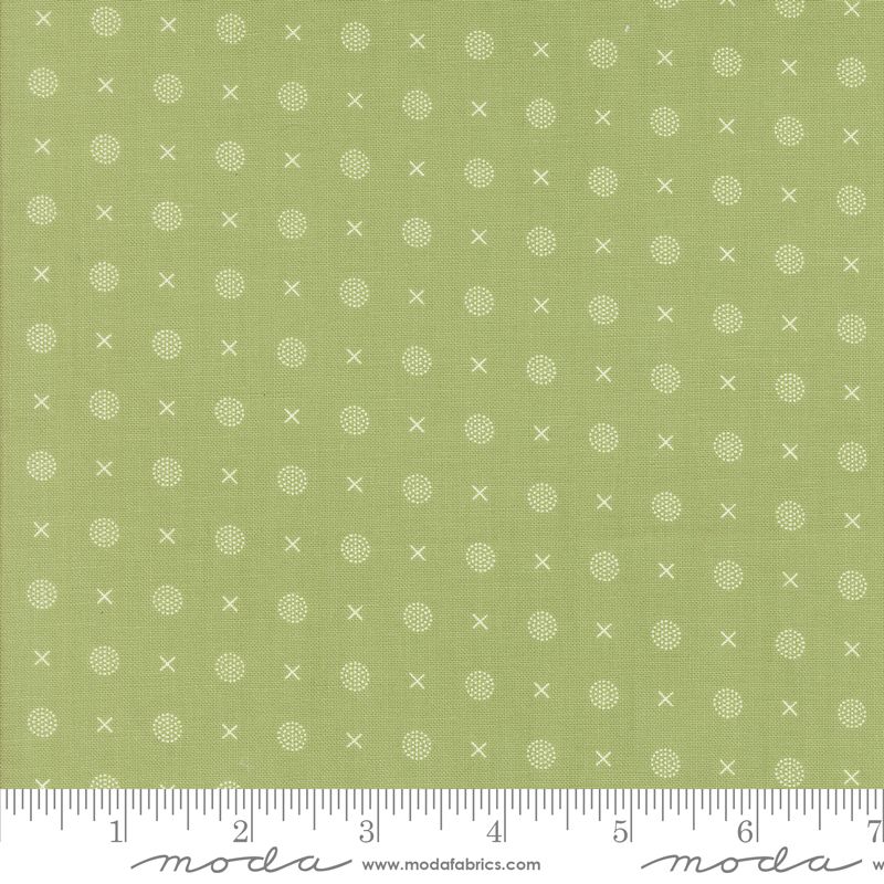 Green fabric with a repeating pattern of small white crosses and dotted circles, shown with a white ruler along the bottom edge.