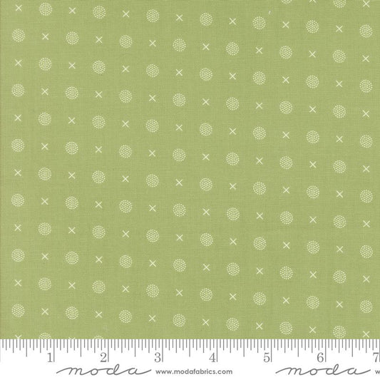 Green fabric with a repeating pattern of small white crosses and dotted circles, shown with a white ruler along the bottom edge.
