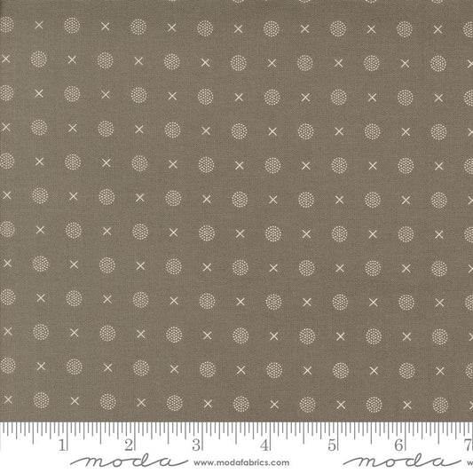 A close-up of a fabric pattern featuring small white x and dot motifs on a slate gray background, with a ruler along the bottom edge showing scale and Modas Fabrics branding.