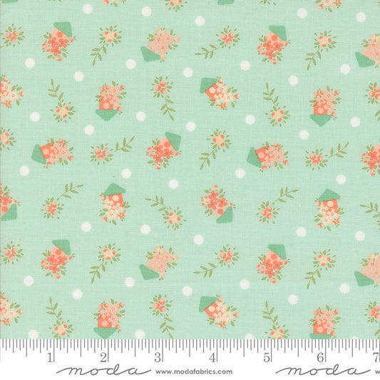 A close-up of a fabric pattern featuring small coral-pink flowers and green leaves in bird houses set against a pale blue background with white polka dots. A white ruler along the bottom edge shows measurements, and the Modas Fabrics logo is printed at the bottom.