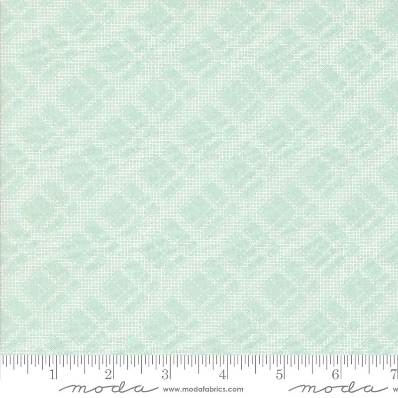 A close-up of a fabric pattern swatch in pale blue with a repeating small geometric diamond motif, plus a measuring ruler along the bottom edge and Moda branding.