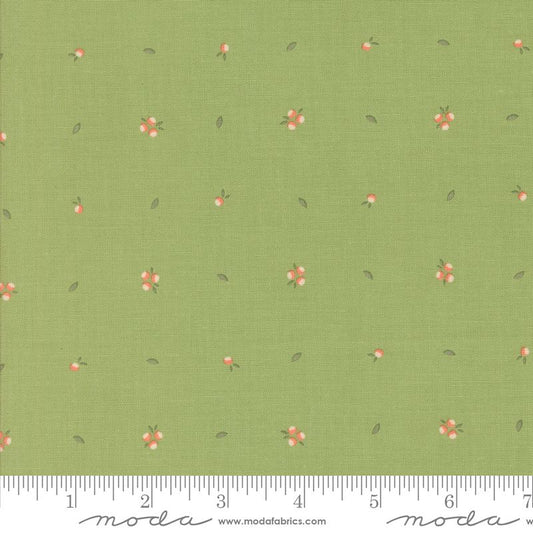 Green fabric with a repeating pattern of small pink flowers, white centers, and tiny green leaves, shown with a measuring ruler along the bottom edge. The brand name 'moda fabrics' is printed on the ruler.