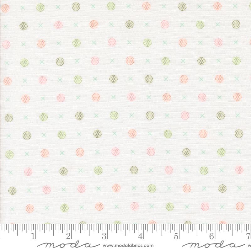 A close-up of a fabric pattern featuring small pink, sage green, and olive polka dots and crosses on a white background, with a measuring ruler along the bottom edge showing the scale.