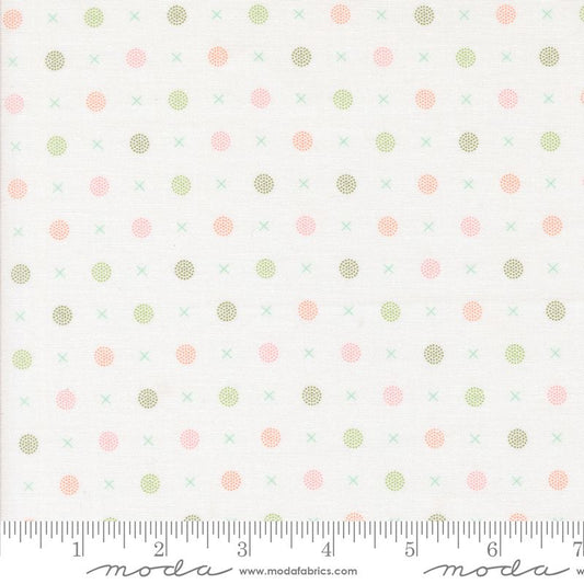 A close-up of a fabric pattern featuring small pink, sage green, and olive polka dots and crosses on a white background, with a measuring ruler along the bottom edge showing the scale.