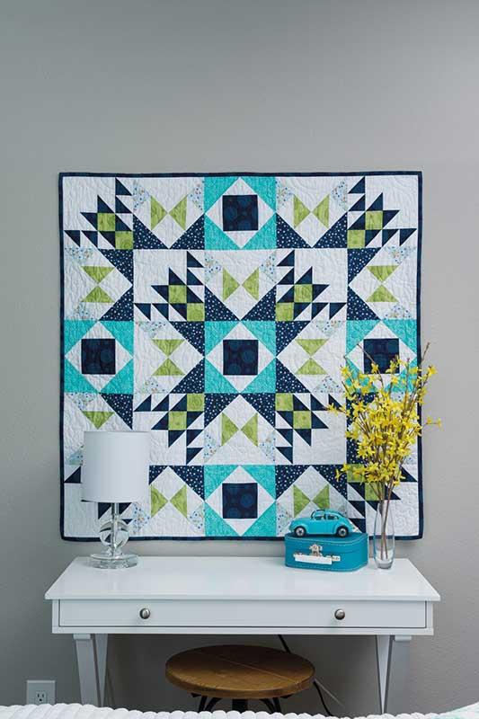 Geometric quilt hanging on a wall above a white console table with decorative items.