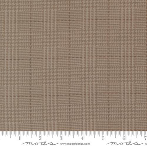 A close-up of a woven fabric texture in a warm taupe-beige color, showing a subtle basketweave or plaid-like weave pattern. A white ruler with inch markings is visible along the bottom edge, and the word 'moda' appears in script near the bottom as a watermark/branding mark.