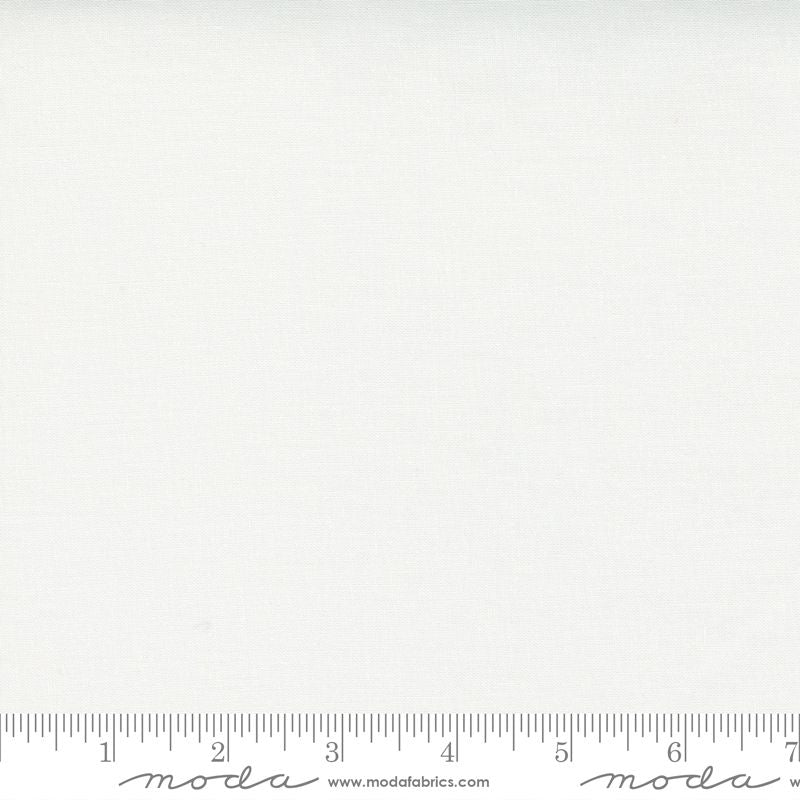 A close-up of a plain white fabric texture with a ruler along the bottom edge for scale, and Moda watermarks across the image.