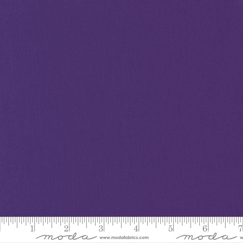 A close-up of a solid purple fabric texture with a white ruler along the bottom edge showing measurement markings and Modra branding.