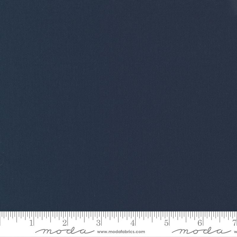 A close-up of a dark navy blue fabric texture with a white ruler along the bottom edge showing measurement markings and Moda branding.