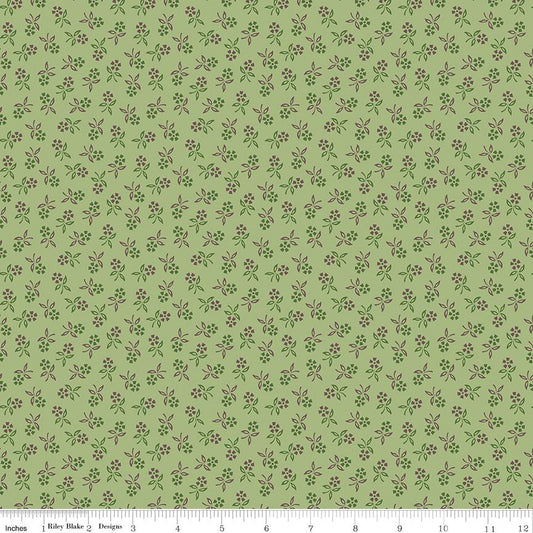 A repeating floral pattern on a light sage green background, featuring small purple and green blossoms. A white ruler at the bottom edge shows the brand 'Riley Blake Designs' and includes inch markings.
