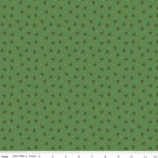A repeating fabric pattern on a muted green background with small dark brown leaf motifs and tiny light dots, shown with a ruler along the bottom edge for scale.