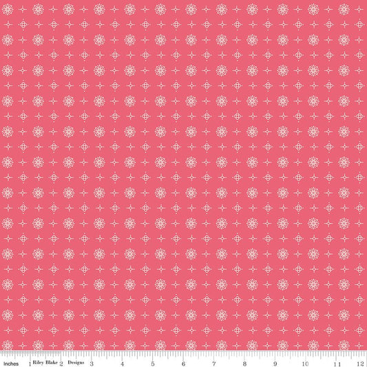 A repeating fabric pattern featuring white snowflakes and small white cross motifs on a solid coral pink background, with a ruler scale at the bottom indicating inches.