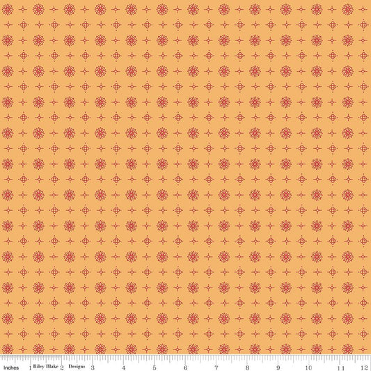 A repeating fabric pattern featuring small red floral medallions interspersed with red plus-sign motifs on a warm gold background. A ruler scale is visible along the bottom edge.