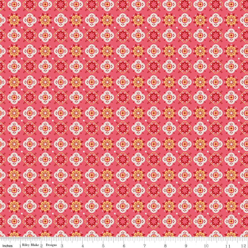 A repeating fabric pattern featuring geometric medallions and floral motifs in coral pink, red, orange, yellow, and white, with a white ruler scale at the bottom indicating inches.