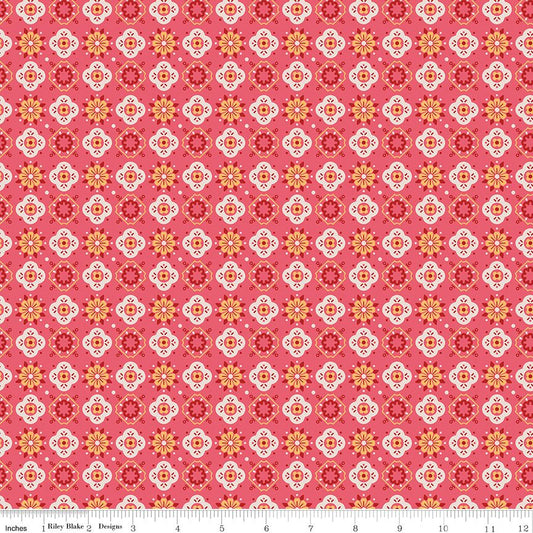 A repeating fabric pattern featuring geometric medallions and floral motifs in coral pink, red, orange, yellow, and white, with a white ruler scale at the bottom indicating inches.